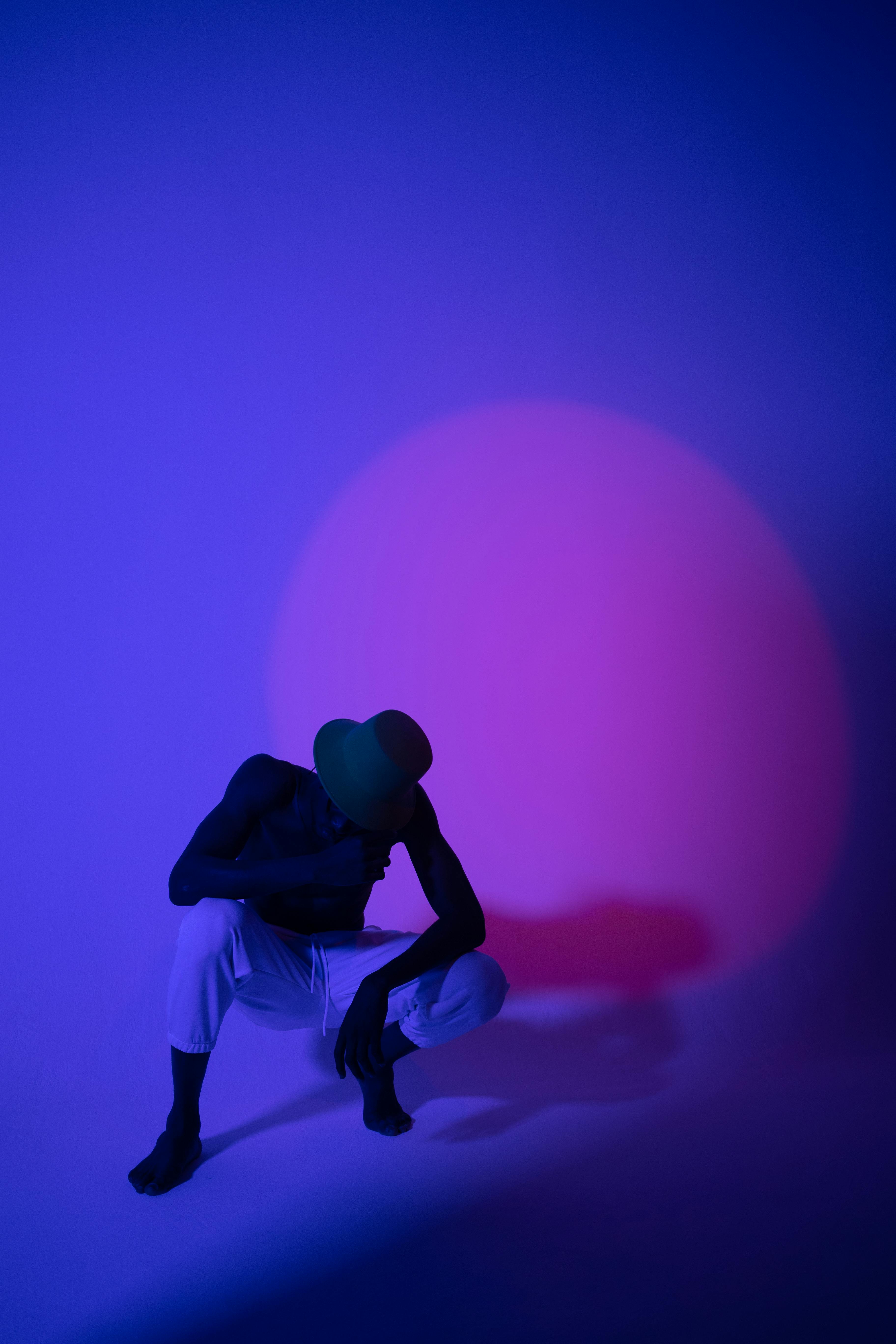 Modern artistic portrait of a crouching man with vibrant lighting in a studio.