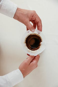 Hands preparing pour over coffee with dripper on white background.