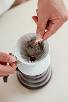 Close-up of a hand placing a coffee bag into a pour over dripper. Perfect for coffee enthusiasts.
