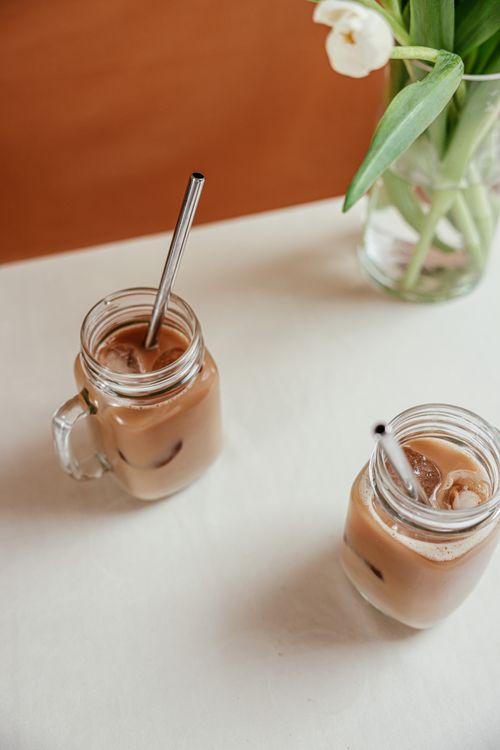 Free Two mason jar glasses of iced coffee with metal straws on a white table. Stock Photo