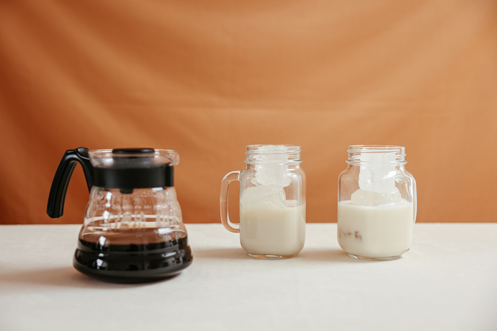 Stylish iced coffee arrangement with milk and coffee pot on a minimalist background.