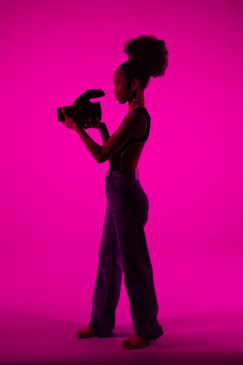 A Woman in Denim Jeans Standing while Holding a Camera