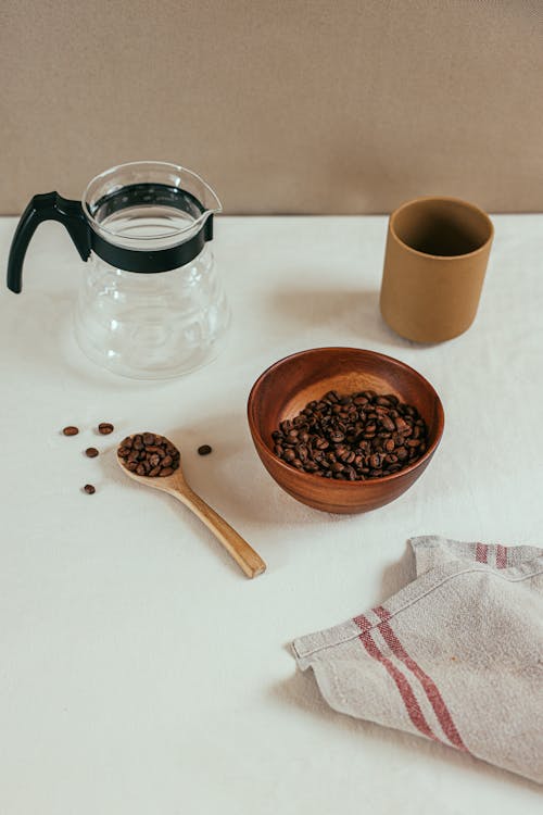 A Bowl of Coffee Beans beside a Coffee Server on a White Table
