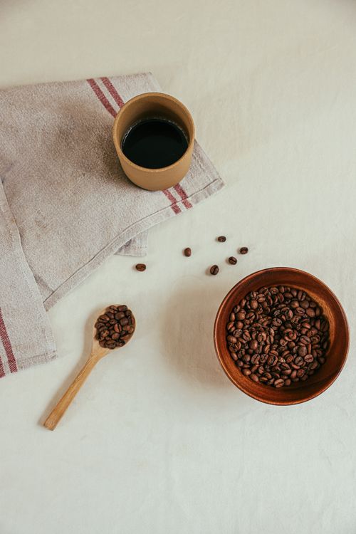 Free A high-angle view of coffee beans in a bowl, a cup of coffee, and a spoon on a cloth napkin. Stock Photo