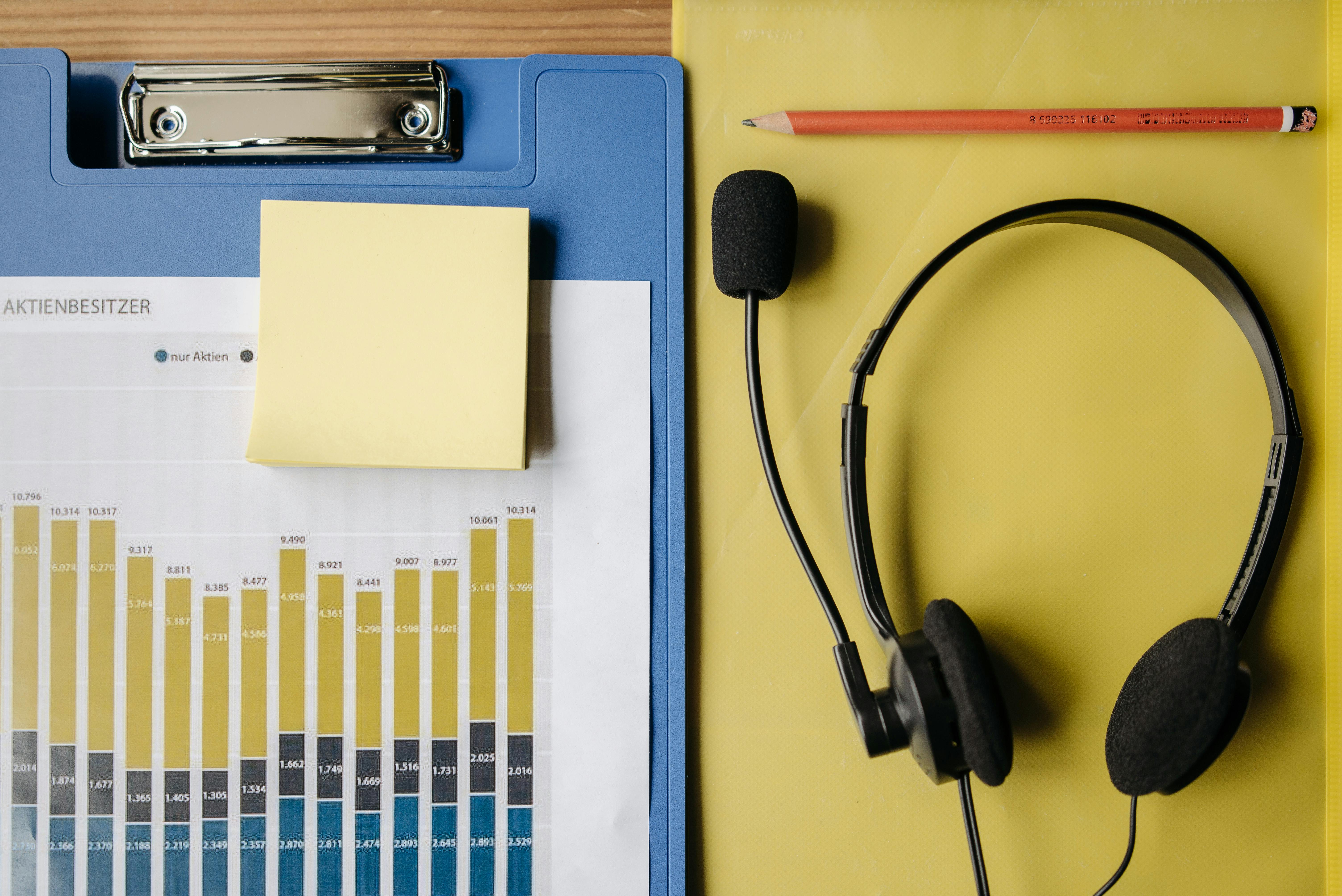 Flat lay of office items including a graph, headset, and stationery on a desk.