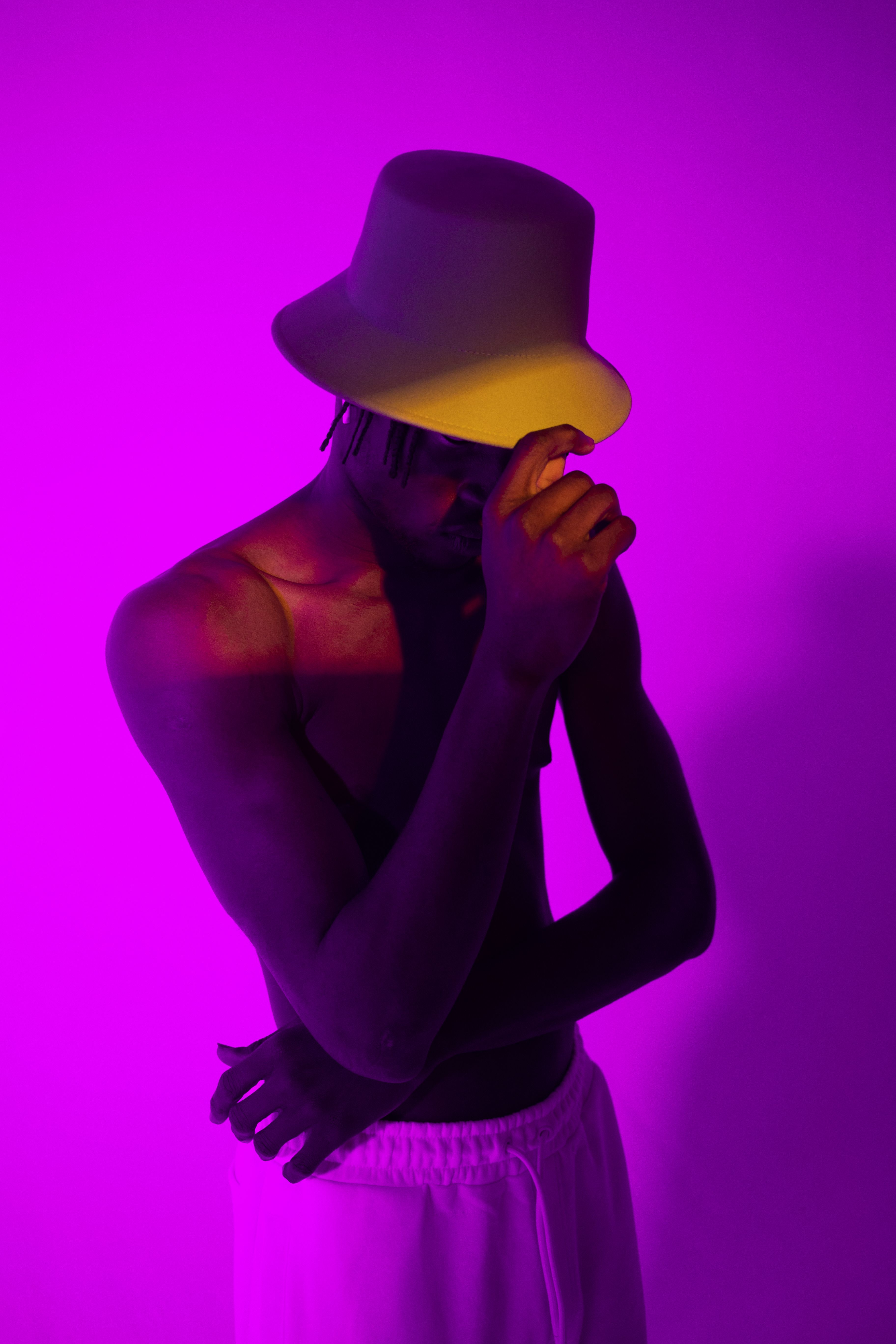 Artistic portrait of a stylish man wearing a hat, illuminated by vibrant purple neon lighting.