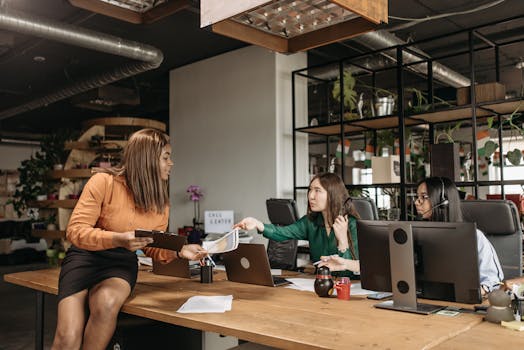 Diverse group of female professionals discussing work at their desk in a modern office setting.