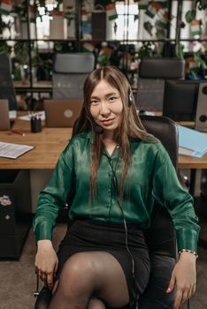 A confident woman in business attire with headphones sitting in a modern office, ready for a meeting.