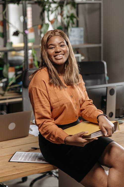 A Woman in Orange Long Sleeve Shirt Sitting on Wooden Table