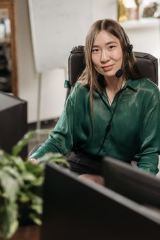 Asian woman smiling while working in a call center office with a headset.