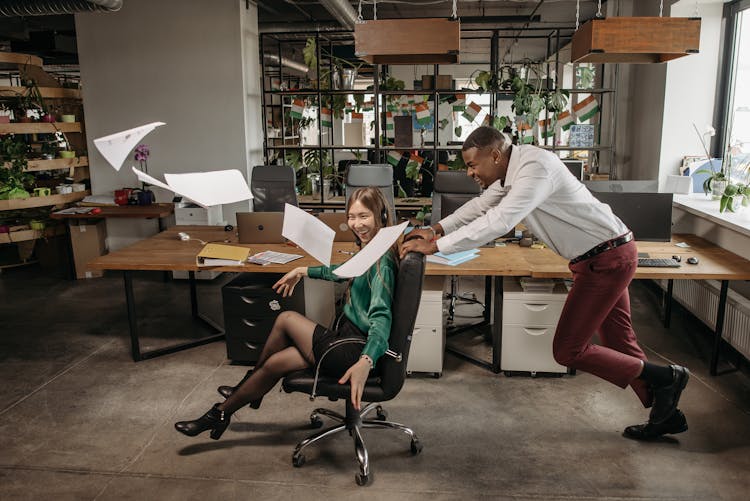 A Man Pushing A Woman Sitting On An Office Chair