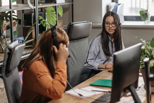 Two women working together in a vibrant office space, wearing headsets and engaging in teamwork.