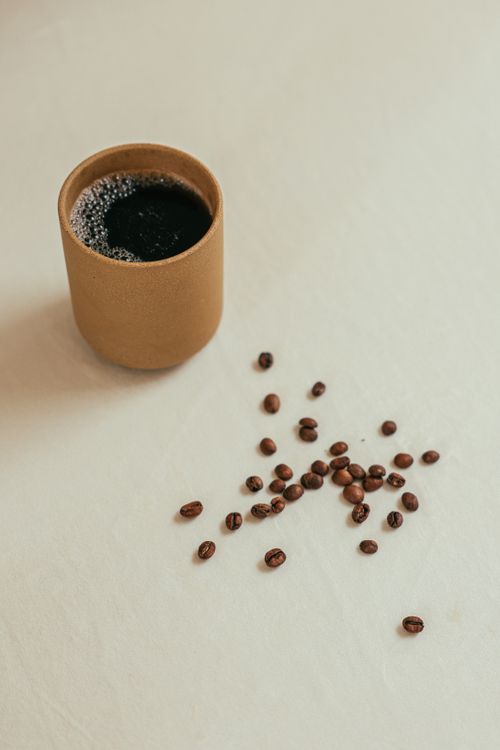 Free A simple cup of coffee with scattered coffee beans on a neutral surface. Stock Photo