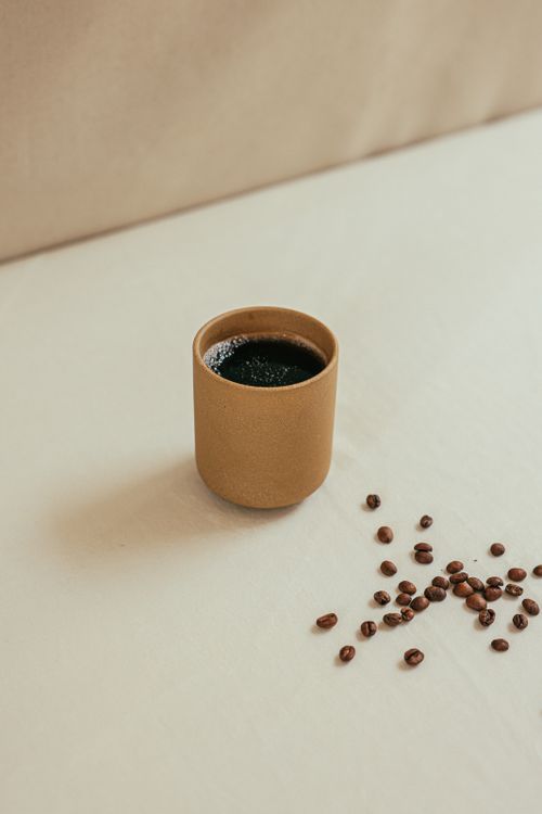 Free A simple clay mug of black coffee with scattered beans on a light background. Stock Photo