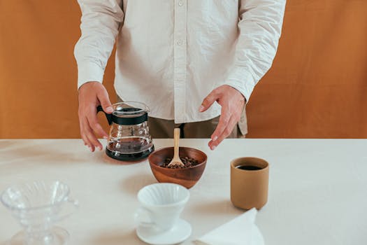 Hands-on coffee brewing with pour over method using a ceramic dripper and fresh coffee beans.