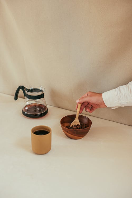 Free Woman Holding a Spoon in a Bowl with Coffee Beans next to a Coffee Pot and a Coffee Cup  Stock Photo