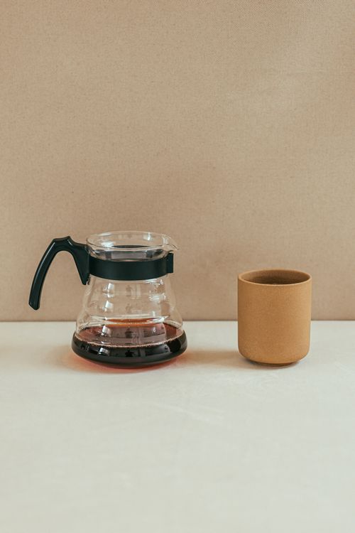 Free A clear glass coffee pot and ceramic mug on a white surface against a neutral backdrop. Stock Photo
