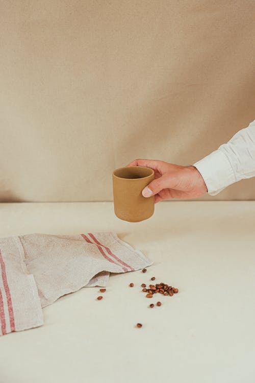 A Person's Hand Holding a Cup of Coffee Near Coffee Beans