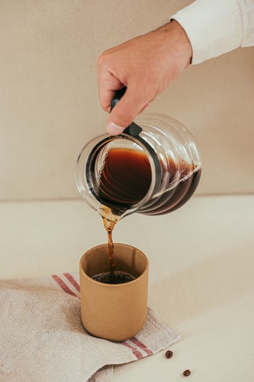 Free A hand pours aromatic filter coffee from a pot into a cup on a white surface. Stock Photo