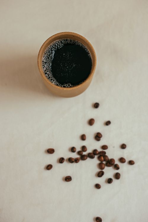 Free Top view of a coffee cup and scattered beans on a neutral surface. Stock Photo
