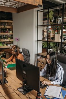 Two women in headsets working diligently in a modern office space with green plants and industrial design elements.