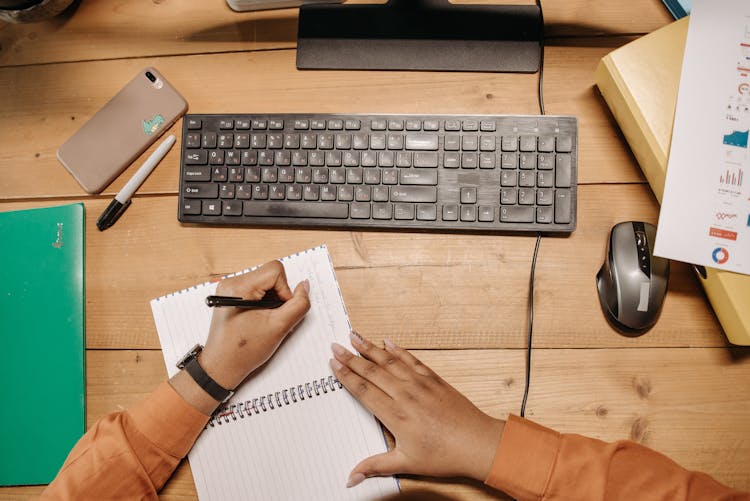 A Person Writing On A Notebook