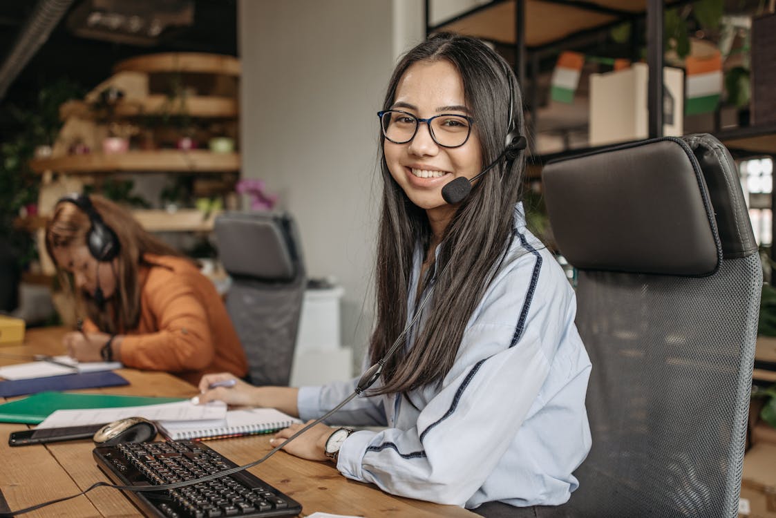 Free A Woman Smiling While Sitting on her Workspace Stock Photo