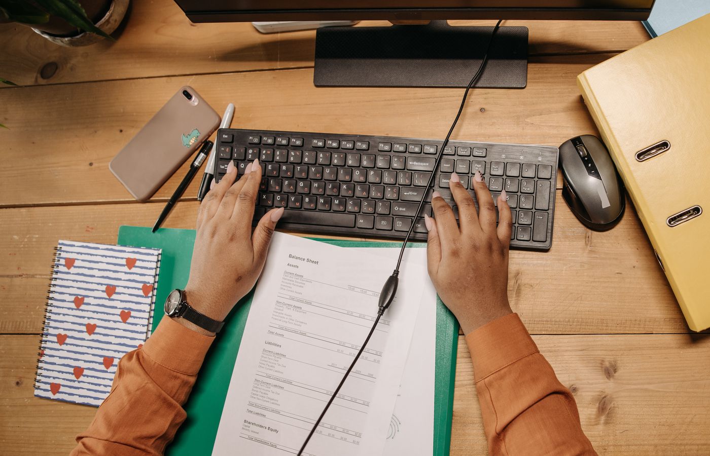 A tidy workspace featuring a keyboard, papers, and office supplies on a wooden desk.