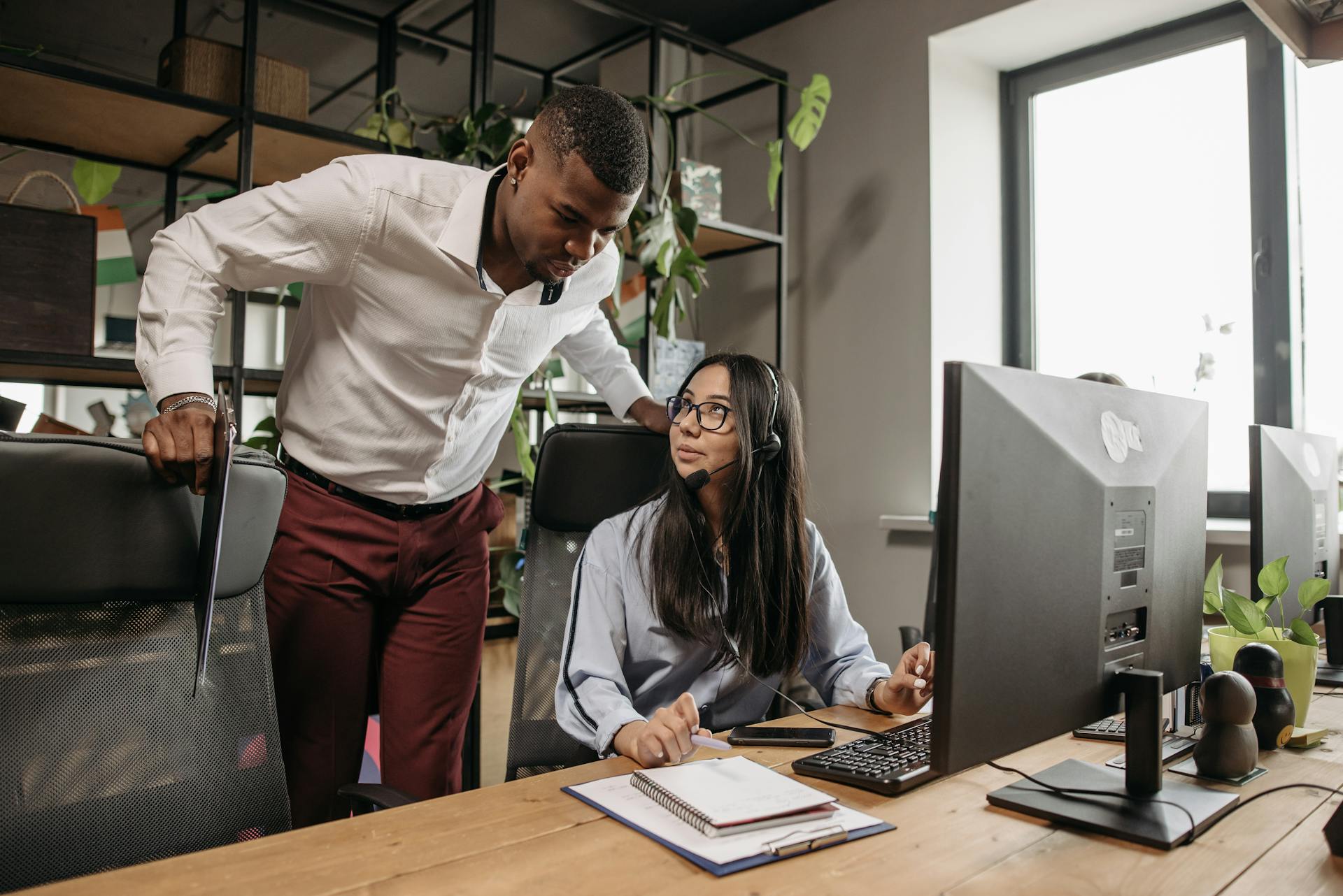 Two colleagues discuss projects at the office with computers and notebooks. Ideal for business and technology themes.