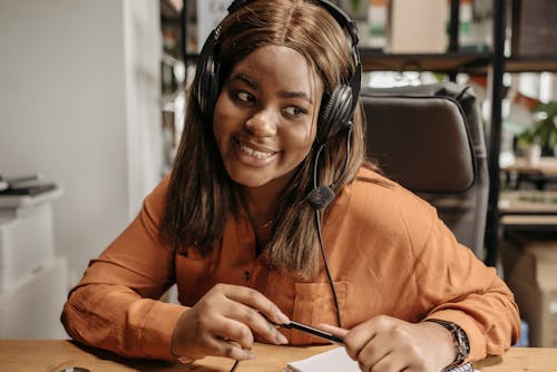 Free Woman in Headphones Holding a Pen and Smiling While Talking Stock Photo