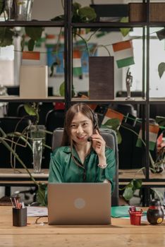 Smiling Asian woman in headset offering customer support services in an office setting.
