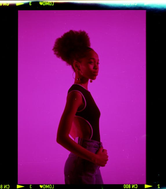 Elegant woman with afro hair posing stylishly against a vibrant purple background, exuding modern fashion.