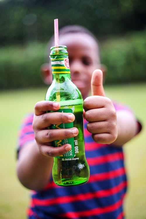 A Child Holding a Bottle with Bubbly Drink Giving a Thumbs Up