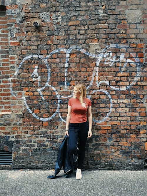 A Woman in Pink Tank Top and Black Pants Standing Beside the Brick Wall