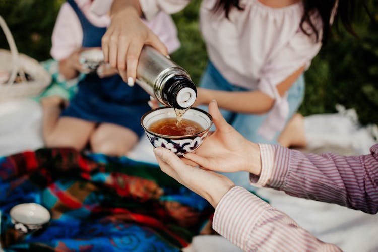 Hand Pouring Tea From Thermos Into Cup During Picnic