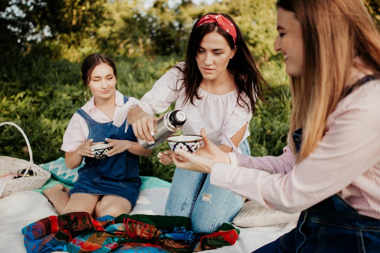 Women Pouring Tea From Thermos On Picnic