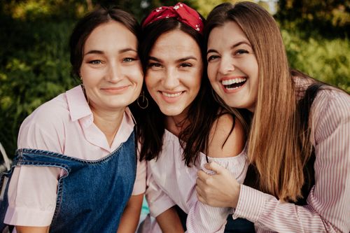 Free Three smiling friends embracing and laughing in a sunny outdoor setting, exuding happiness and friendship. Stock Photo