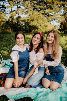 Three women sitting on a blanket enjoying a sunny picnic day together.