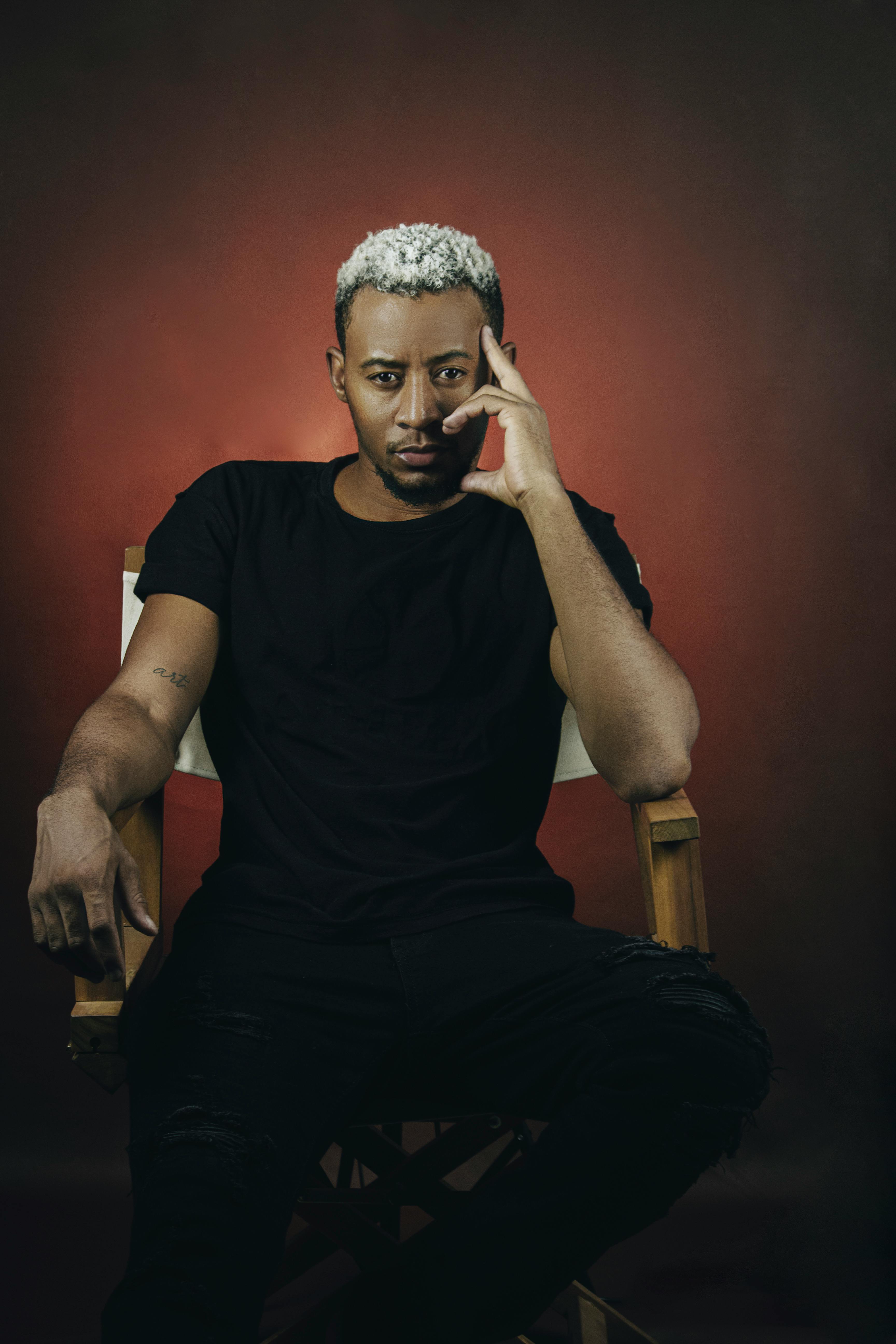 Studio portrait of a confident man with blond hair, black shirt, and thoughtful pose.