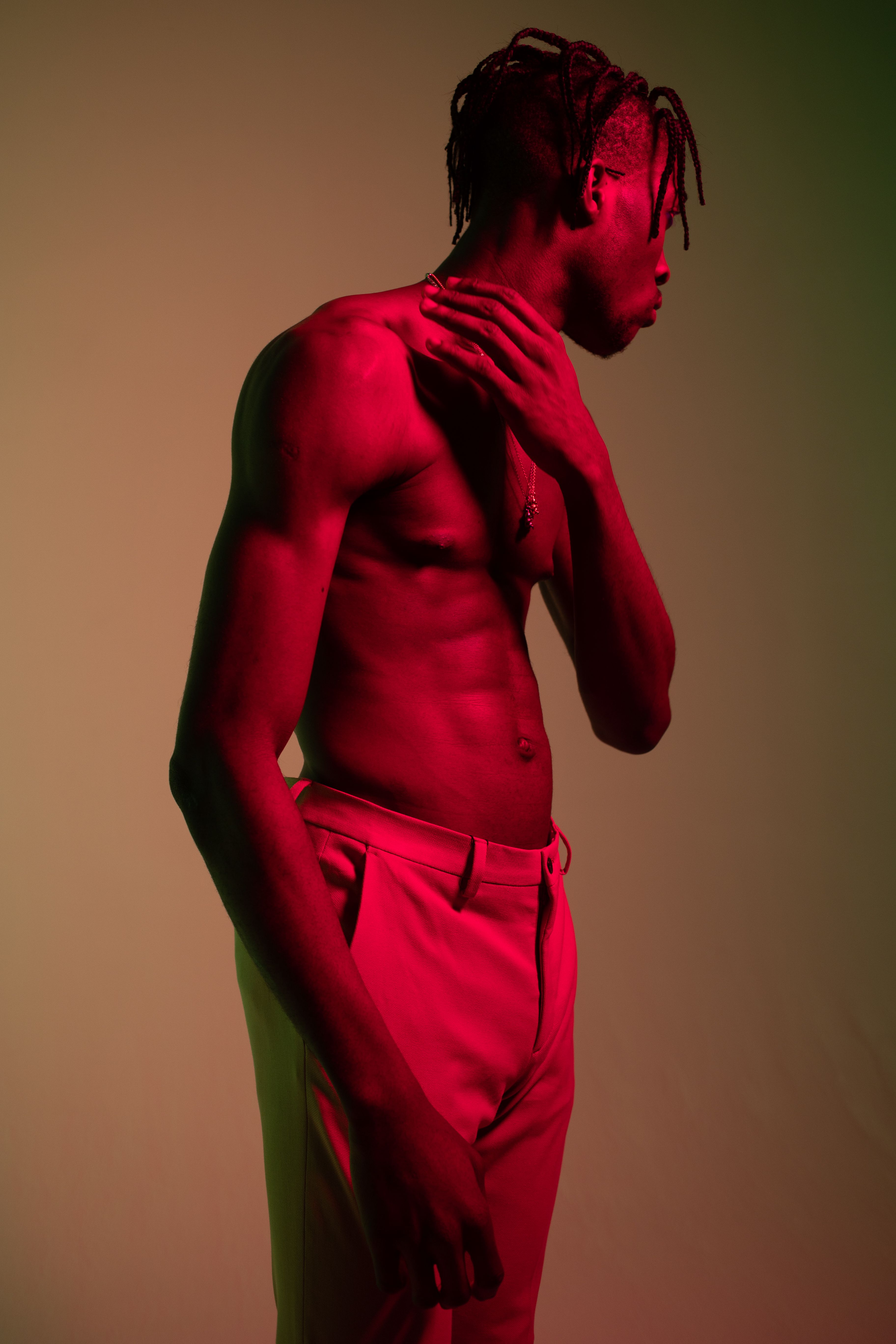 A topless man posing with dramatic red lighting in a studio setting, showcasing artistic expression.