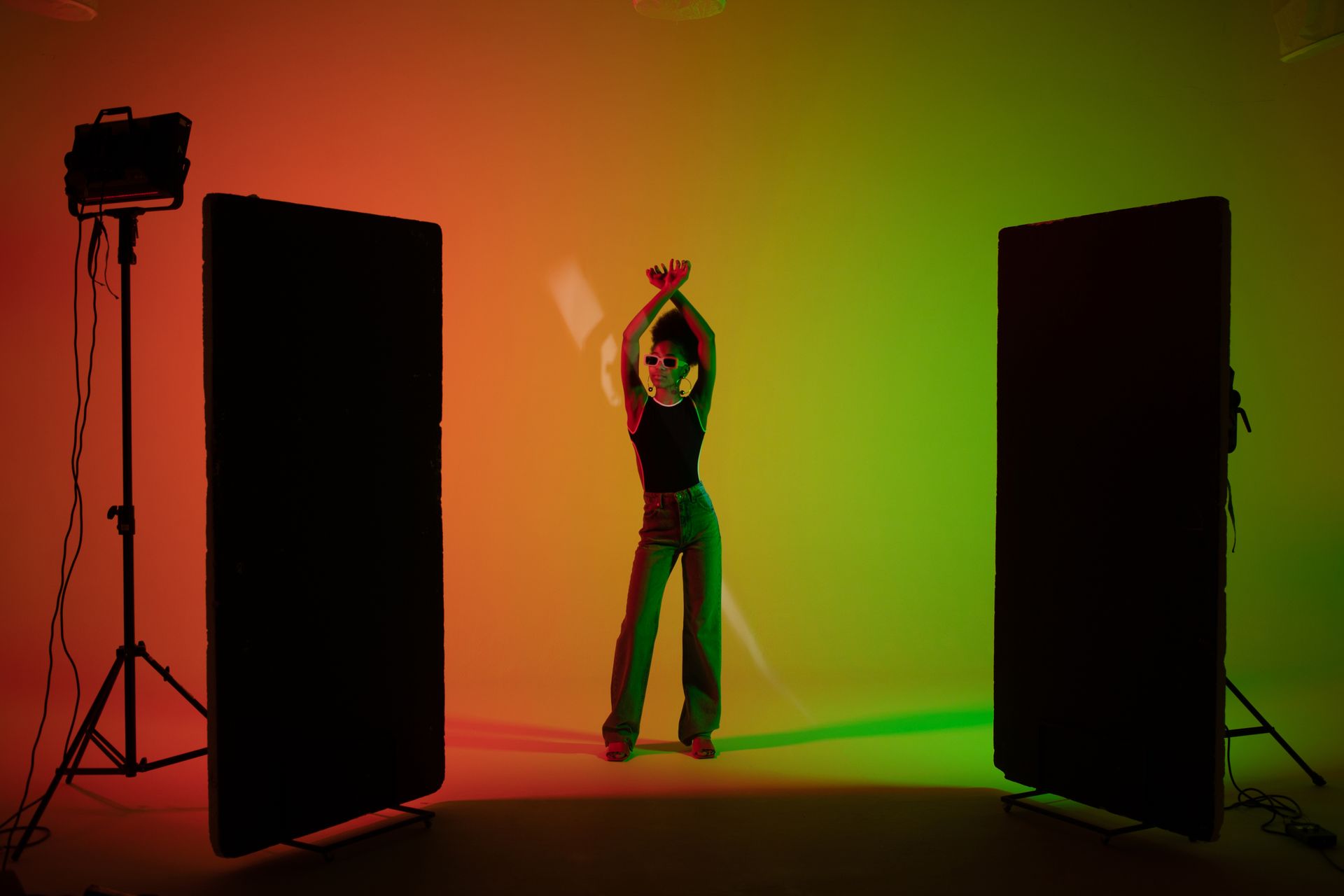 Stylish black woman posing in colorful studio setup with dramatic lighting and shadow effects.