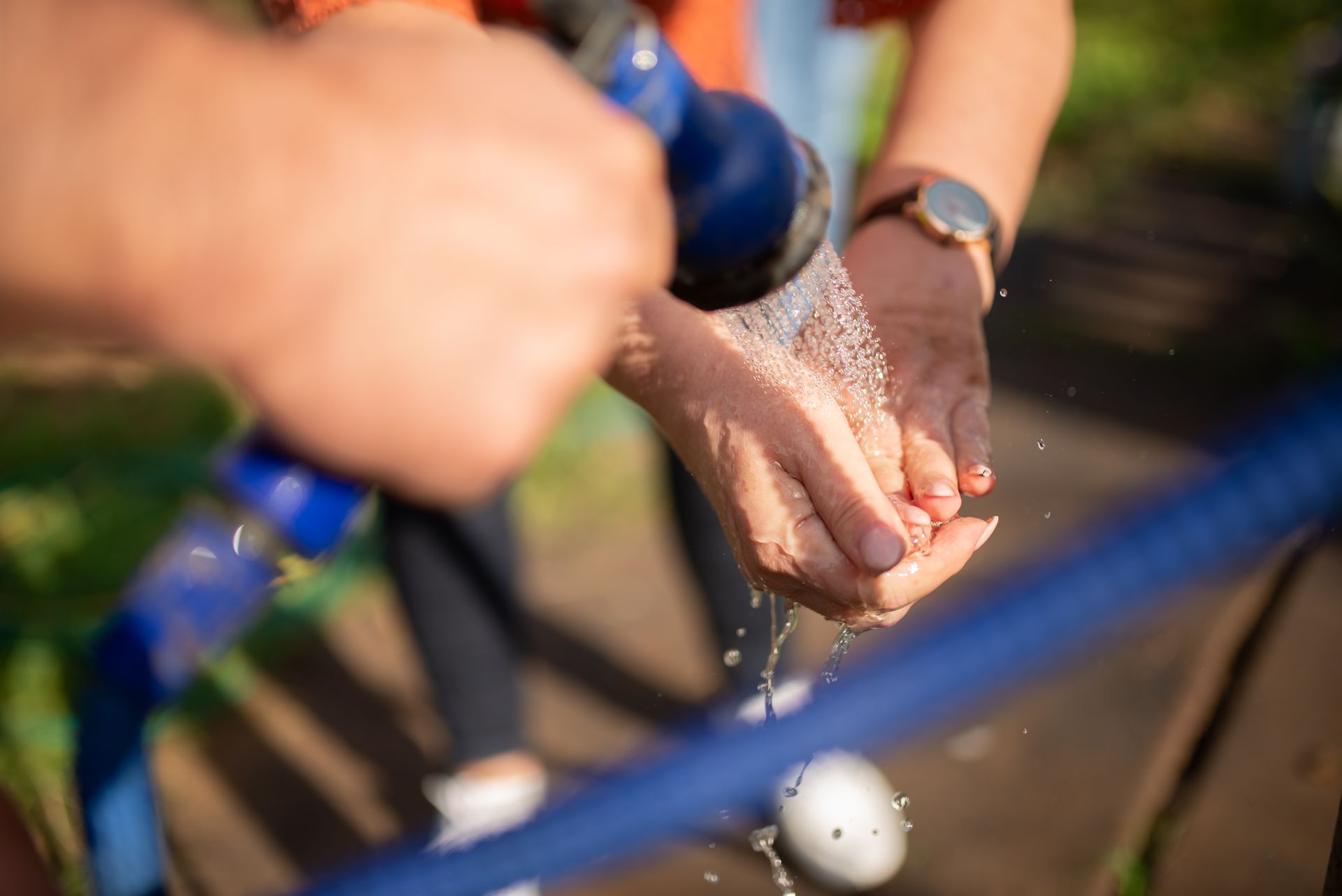 Close-up of hands being washed with a sprinkler hose, emphasizing outdoor cleanliness.