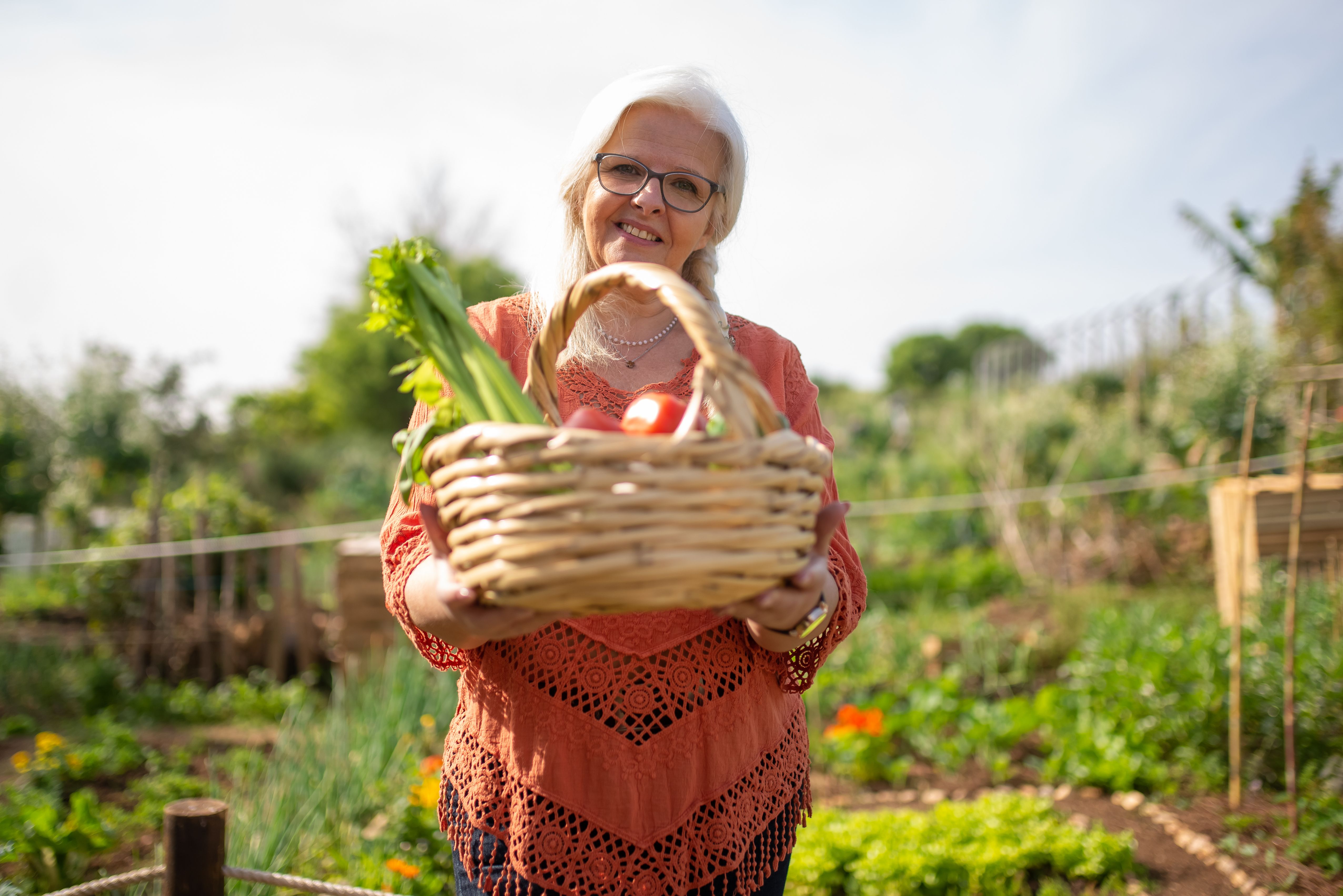 Elderly woman smiling with a basket of fresh vegetables