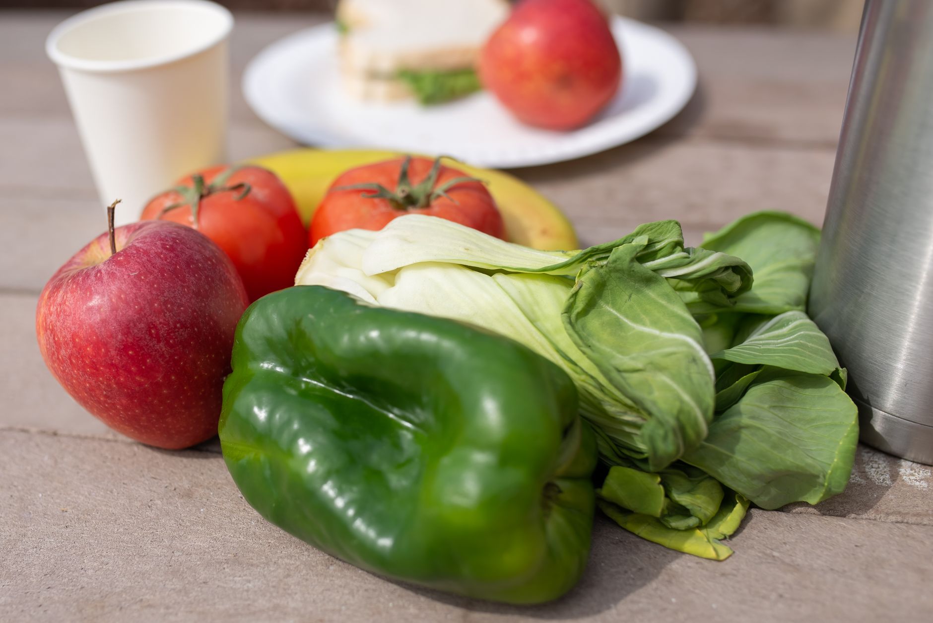 A close-up of vibrant fresh produce including apples, bell peppers, and tomatoes on a wooden table.