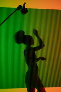 Elegant silhouette of a woman posing against a vibrant green and orange studio background.