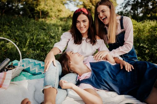 Free Three young women laughing and relaxing during a sunny picnic in the park. Stock Photo