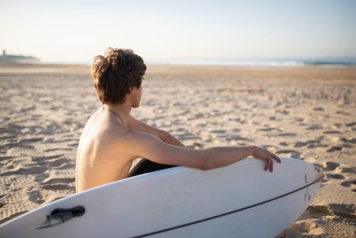 Free Shirtless man with surfboard enjoying a sunny day on a sandy beach. Stock Photo