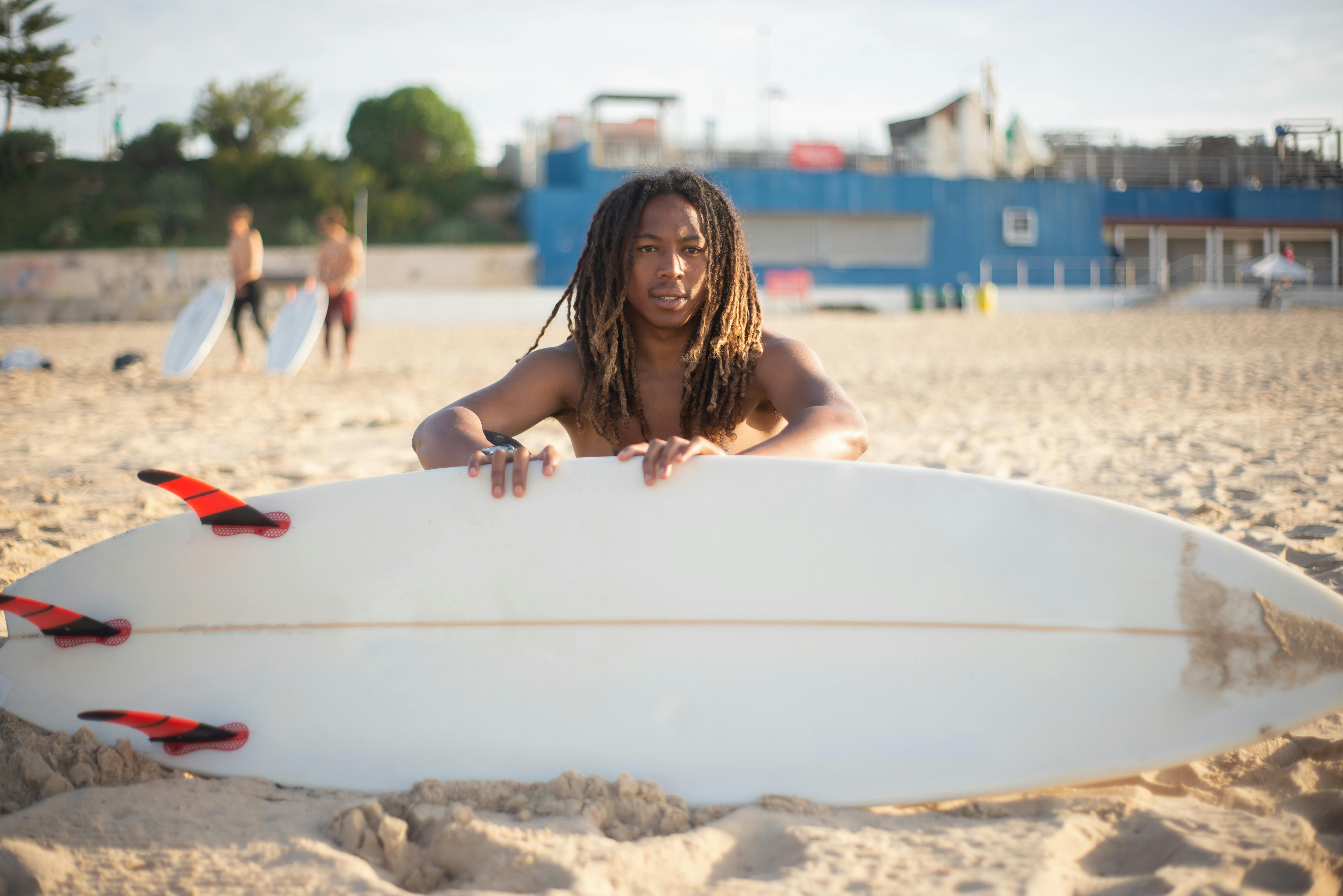 一个长着辫子的非裔美国人在葡萄牙的沙滩上拿着冲浪板