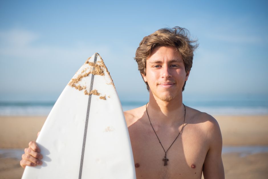 Young shirtless man holding a surfboard on a sunny beach in Portugal, summer vibes.