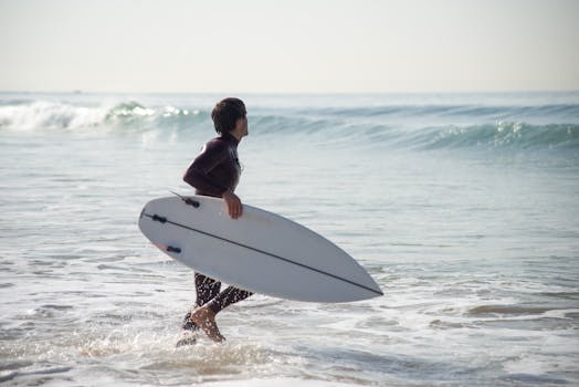 A surfer holding a surfboard walks into the ocean waves at a Portuguese beach during summer.